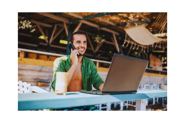 Um nômade digital trabalhando em um laptop em uma praia exótica, em um bar, super tranquilo e alegre, representando a liberdade e a flexibilidade do trabalho remoto