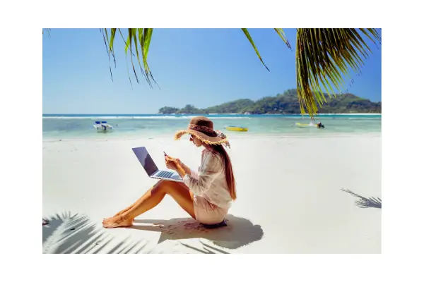 Nômade digital trabalhando em um laptop com vista para o mar, representando o equilíbrio entre trabalho remoto e viagens pelo mundo