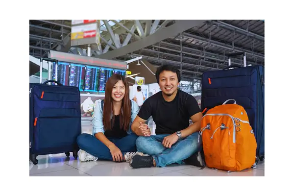 Casal jovem no aeroporto com malas e passaportes, prontos para embarcar em uma viagem, simbolizando planejamento financeiro para viagens