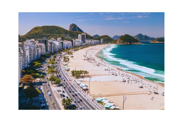 Vista panorâmica do Pão de Açúcar e da Praia de Copacabana ao pôr do sol, com pessoas caminhando no calçadão no Rio de Janeiro em 2025