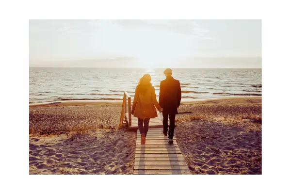 Casal sorridente de mãos dadas, explorando um destino romântico ao pôr do sol, simbolizando uma viagem a dois com paisagem natural ao fundo