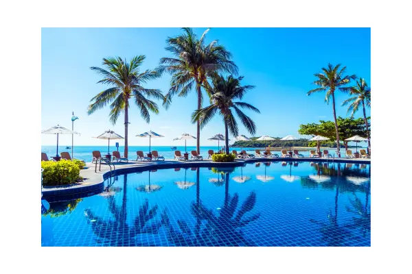 Piscina em pousada à beira-mar em Porto de Galinhas com coqueiros e céu azul, mostrando conforto e natureza.